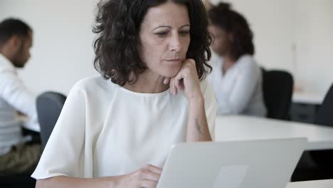 Front-view-of-thoughtful-woman-using-laptop-in-office